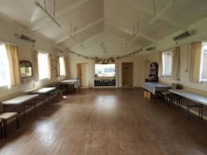 Spacious village hall interior with wooden flooring, large windows, and decorated with bunting for events.